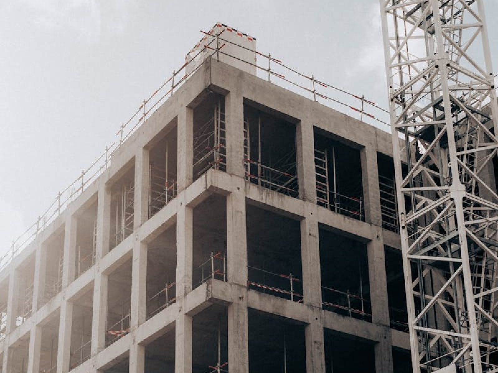 Concrete structure of a multistory building with adjacent crane under cloudy sky.