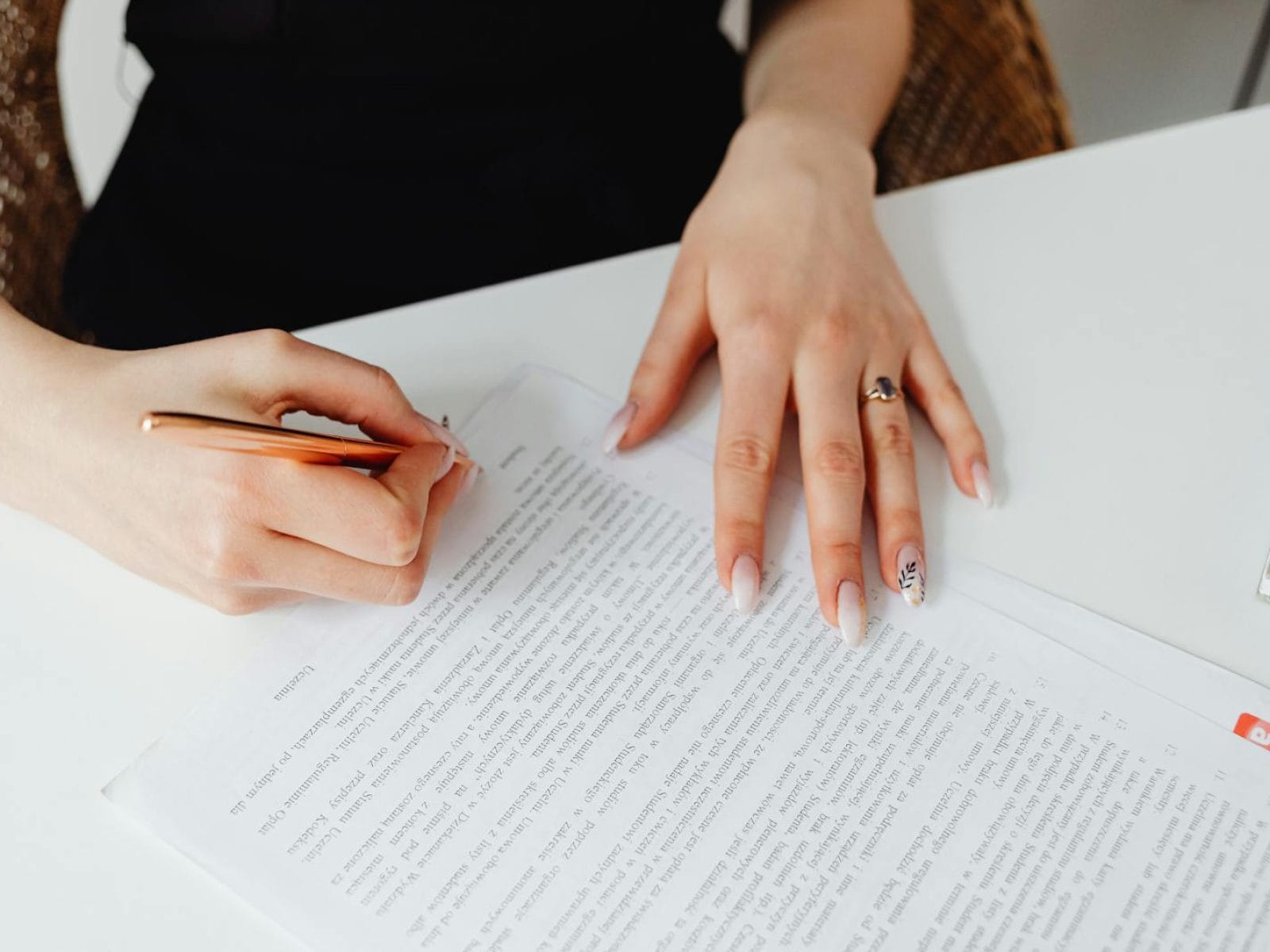 A woman signing a document with a pen on a desk, emphasizing hands and writing.