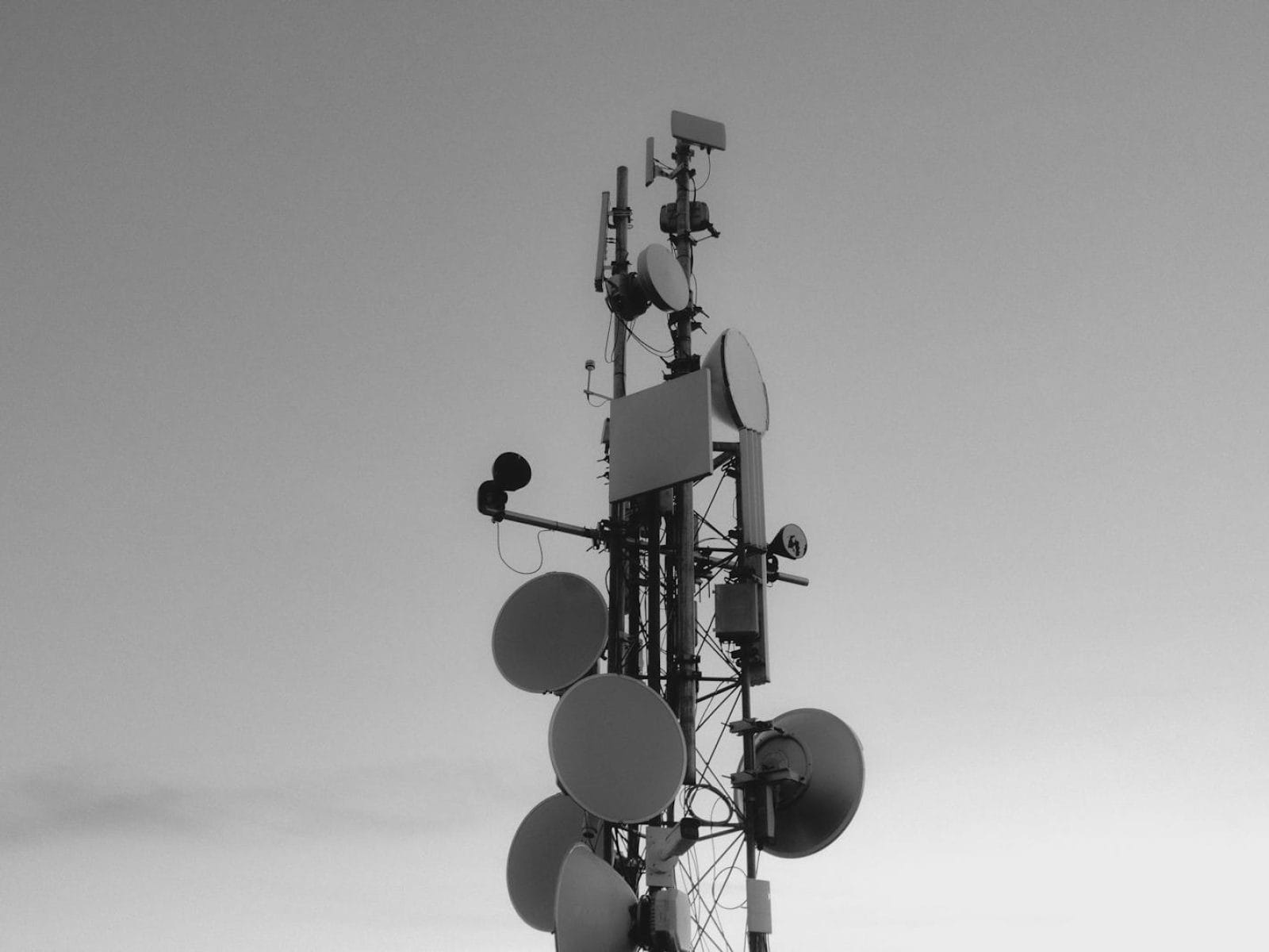 Monochrome image of a tall communications tower with satellite dishes under an expansive sky.