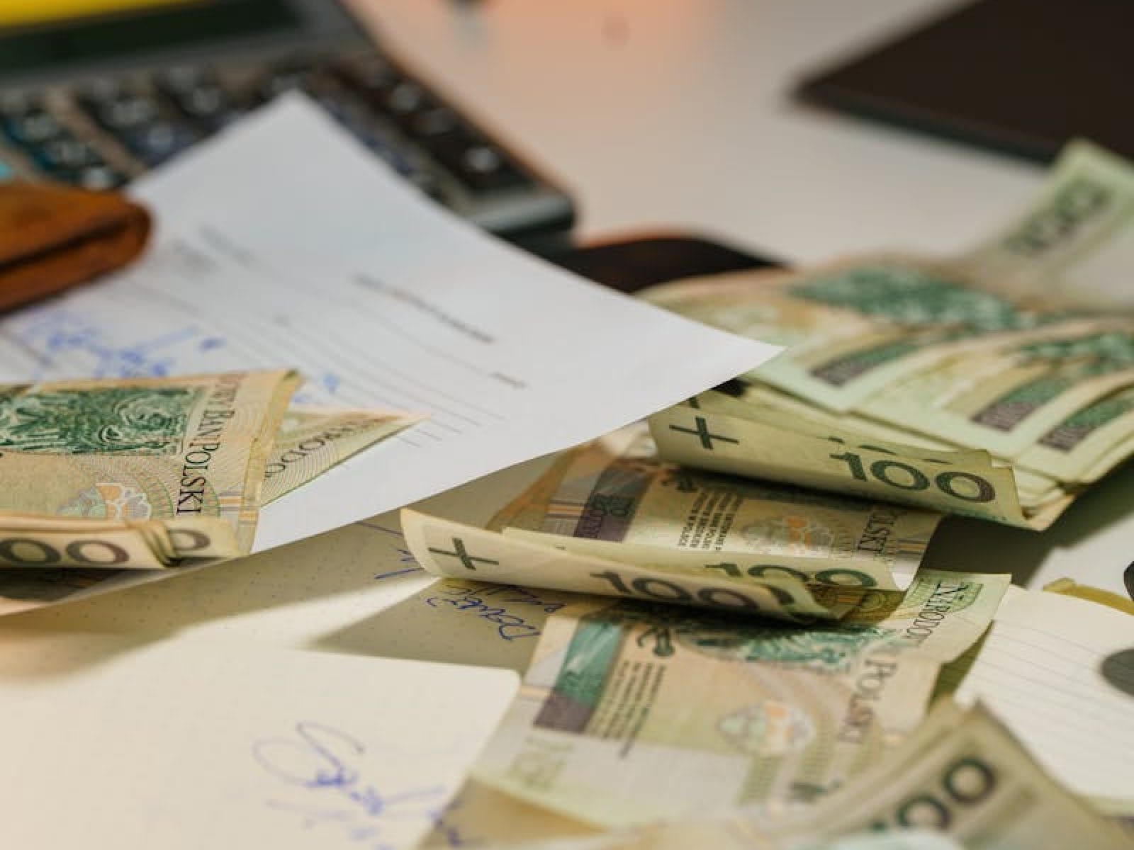 Scattered Polish zloty banknotes with financial documents on an office desk.