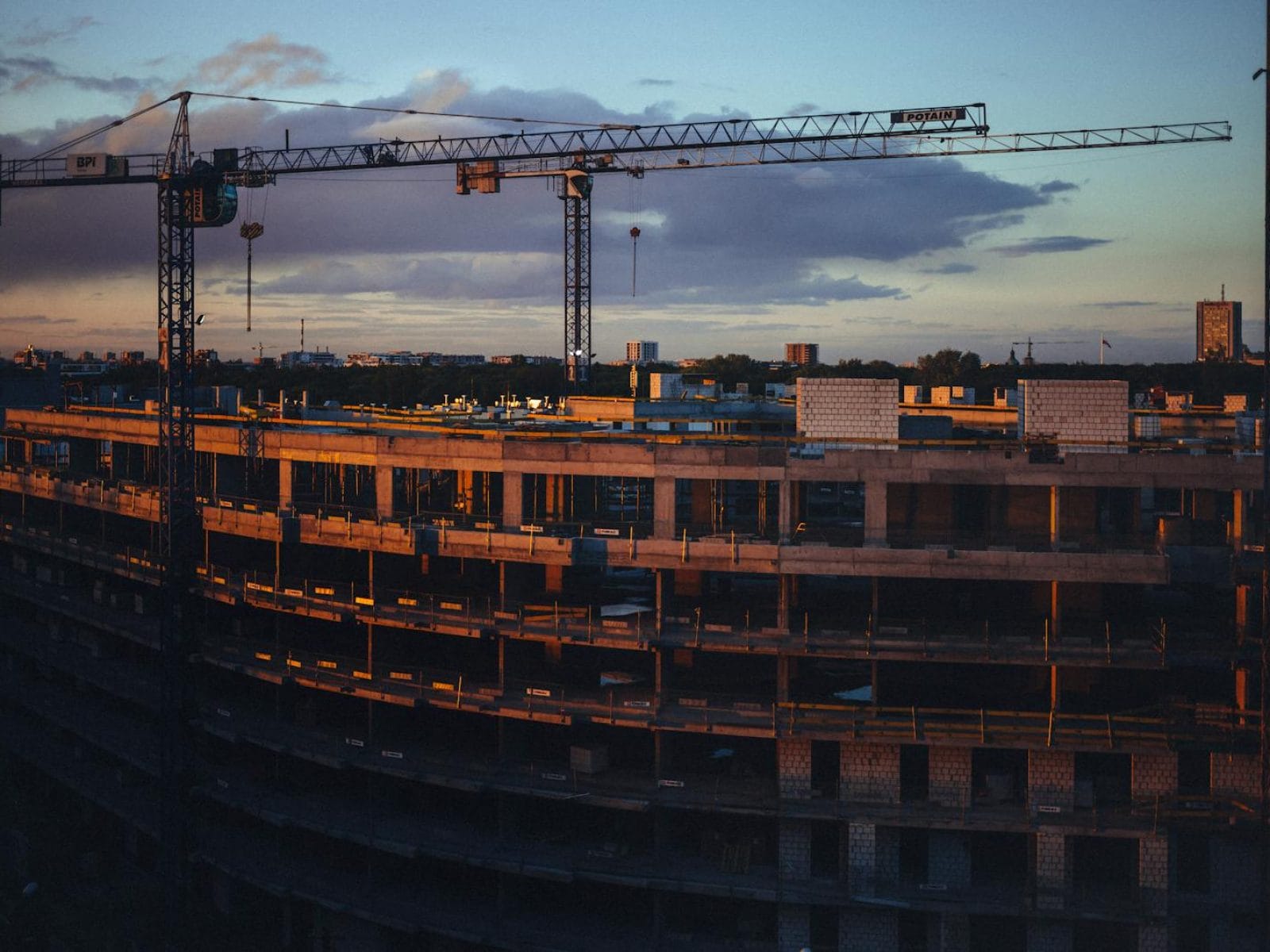 A construction site at sunset featuring cranes and a building under development.
