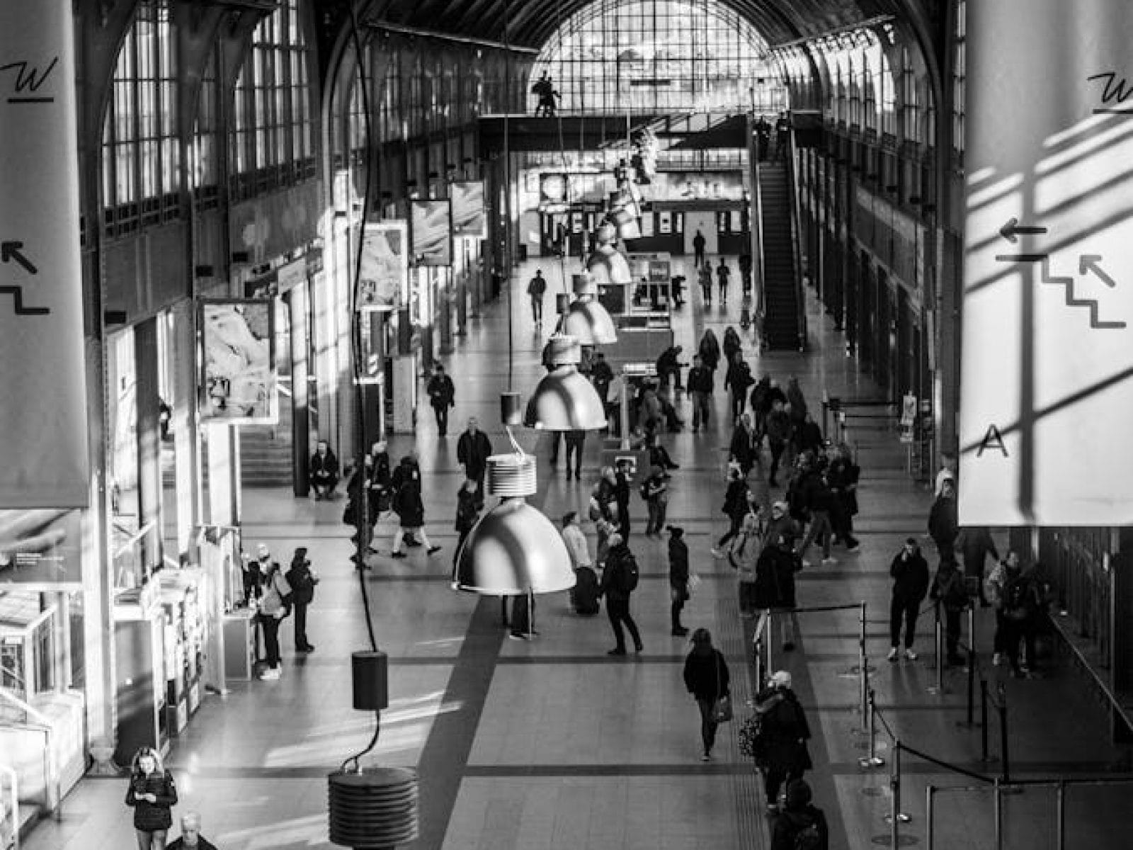 People bustling inside Wroclaw Train Station with arched glass roof.