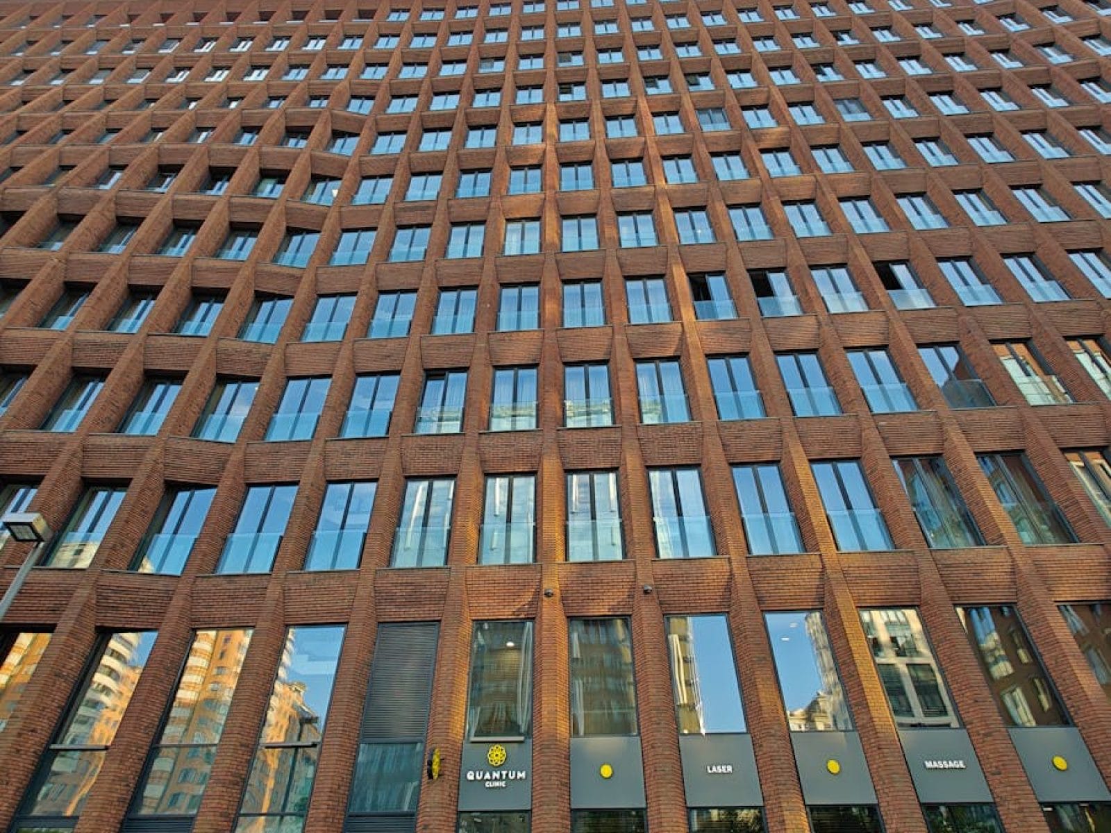 Upward view of a modern brick building with reflective glass windows and clear blue sky.