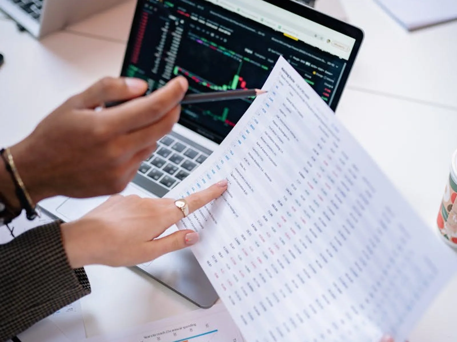 Hands holding documents analyzing data on a laptop in a collaborative office setting.